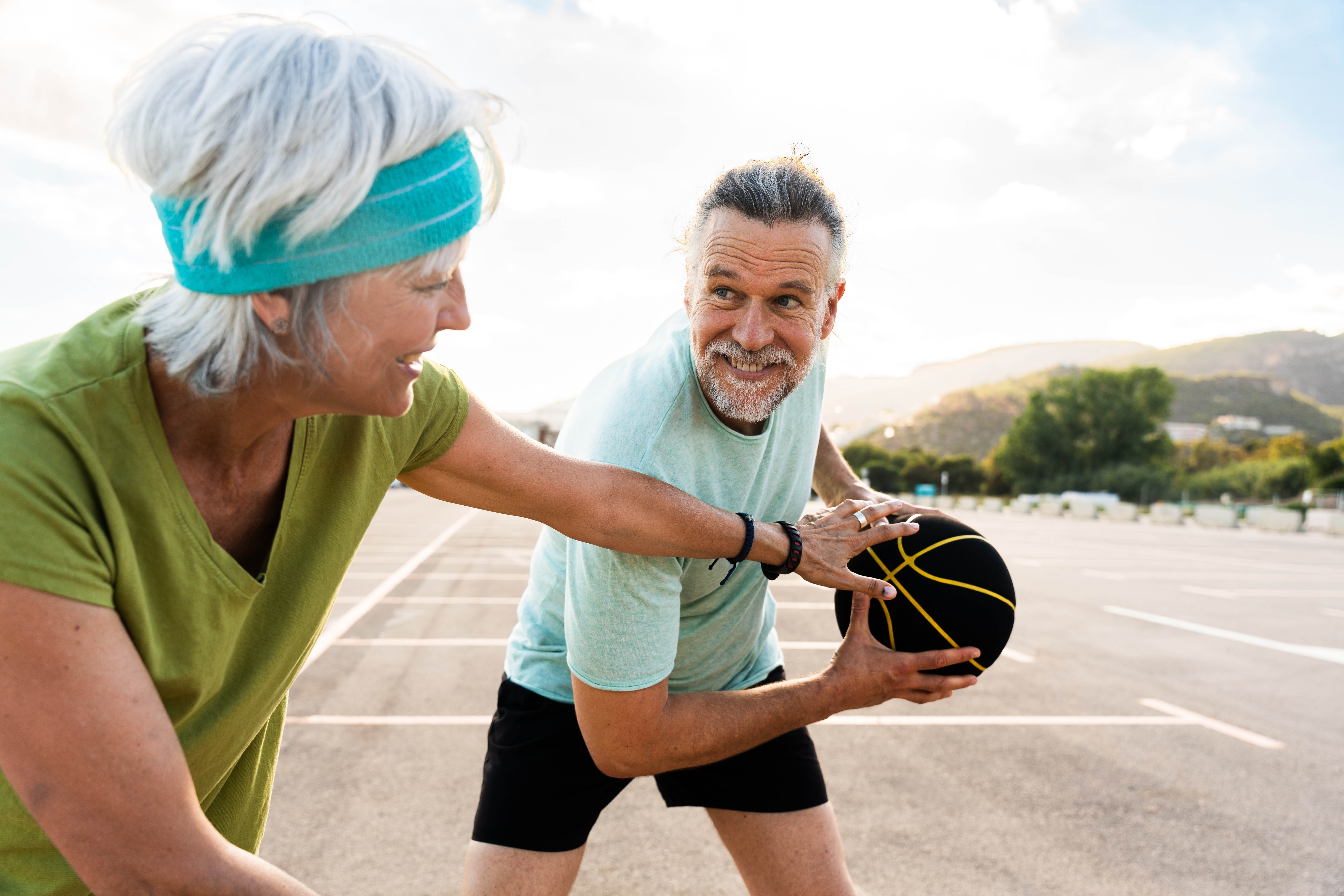 Older man and woman playing basketball on an outdoor court Older man and woman playing basketball on an outdoor court